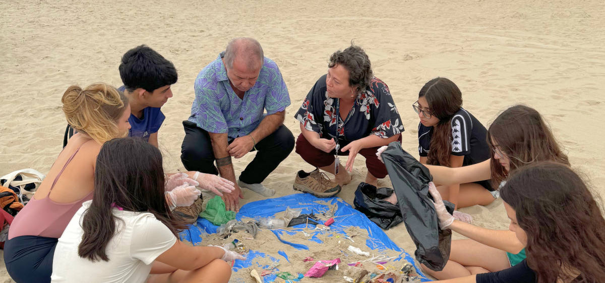 Estudantes do Colégio São Vicente de Paulo participam de uma aula ao ar livre sobre sustentabilidade, analisando resíduos coletados na praia para compreender os impactos ambientais do descarte inadequado.